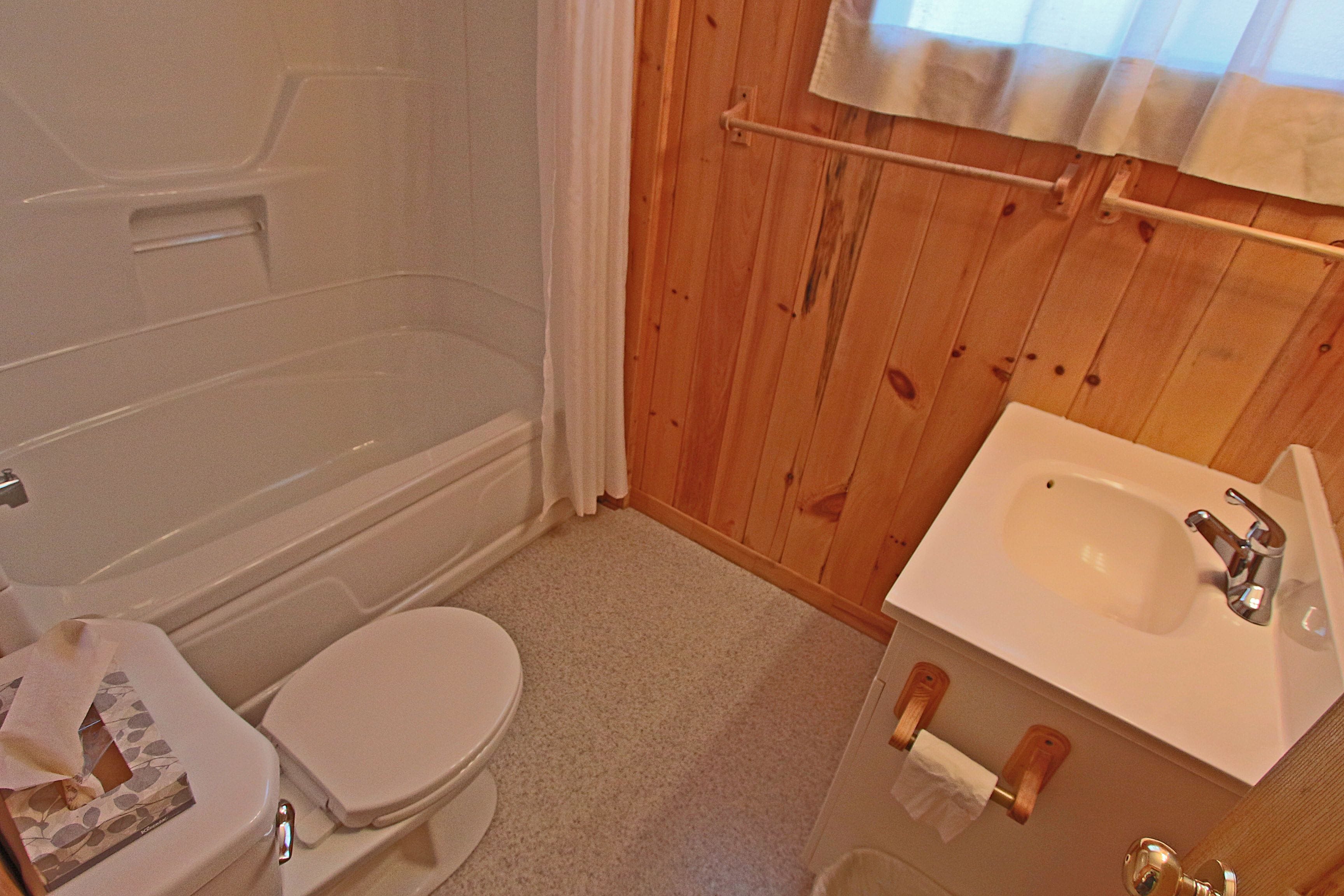 A bathroom with a bathtub, toilet, sink, and wooden walls.