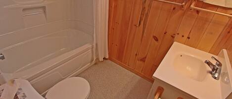 A bathroom with a bathtub, toilet, sink, and wooden walls.