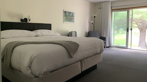 Ein Hotelzimmer mit einem großen Bett, einem Sessel, einem Schreibtisch und Blick ins Freie.