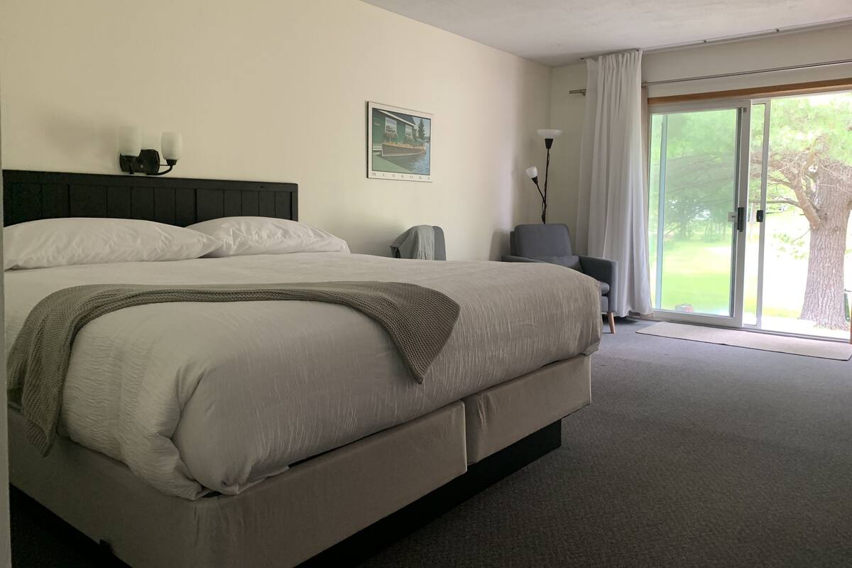 A hotel room with a large bed, a chair, a desk, and a view of the outdoors.