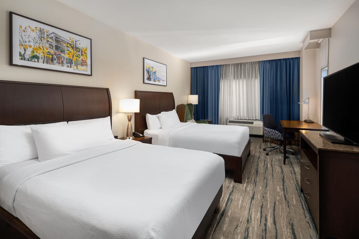 A hotel room with two beds, a desk, a television, and artwork on the walls.