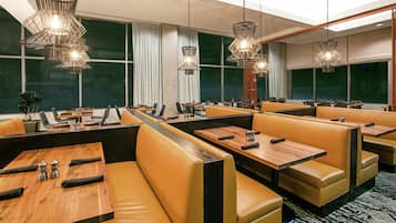 Restaurante com assentos em couro, mesas de madeira e luminárias pendentes.