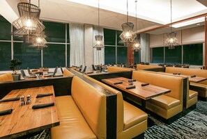 A restaurant with leather booths, wooden tables, and hanging pendant lights.