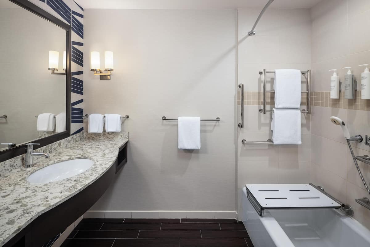 A modern bathroom with a sink, mirror, towel rack, shower, and toiletries.