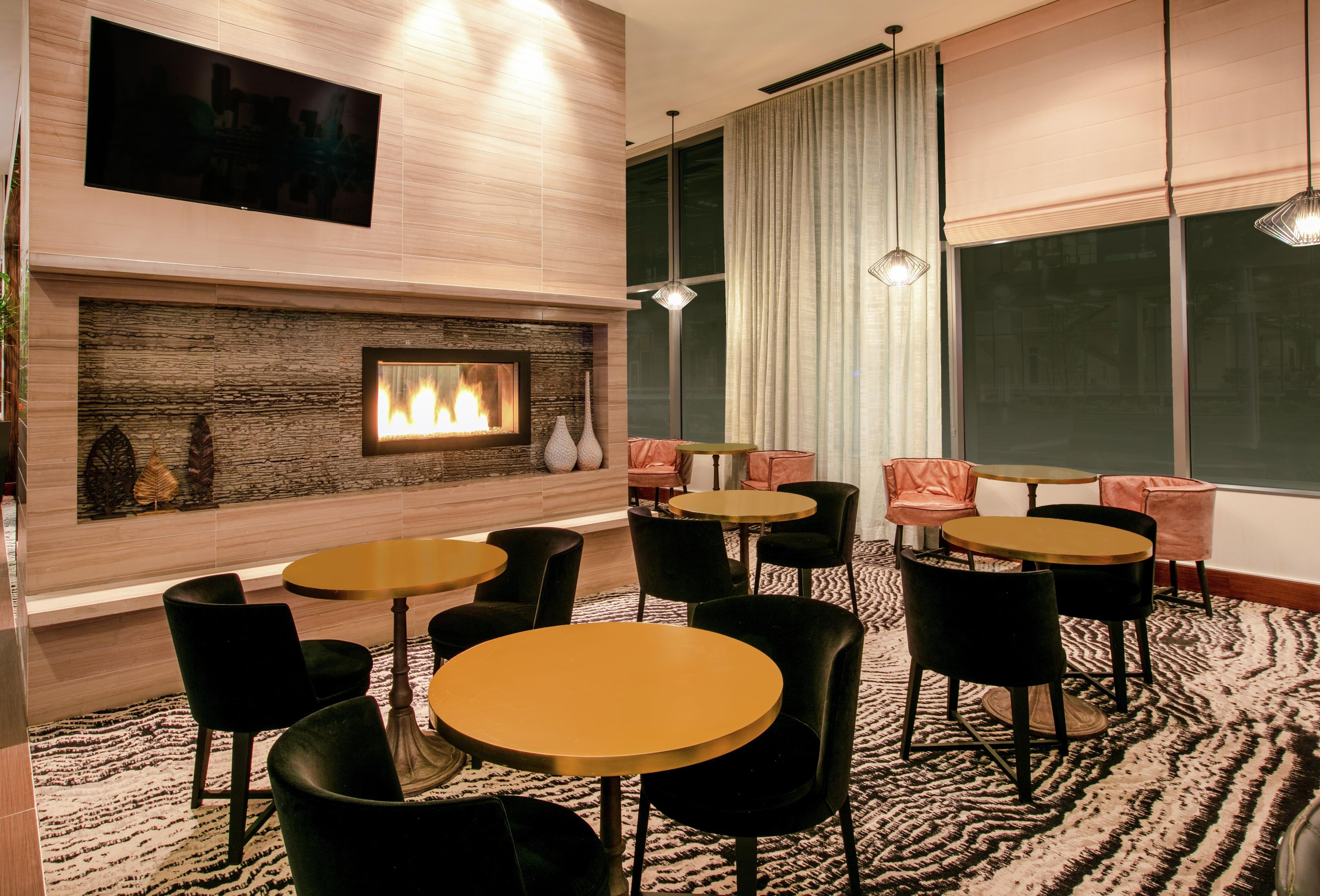A modern lounge area with a fireplace, multiple seating arrangements, and large windows.