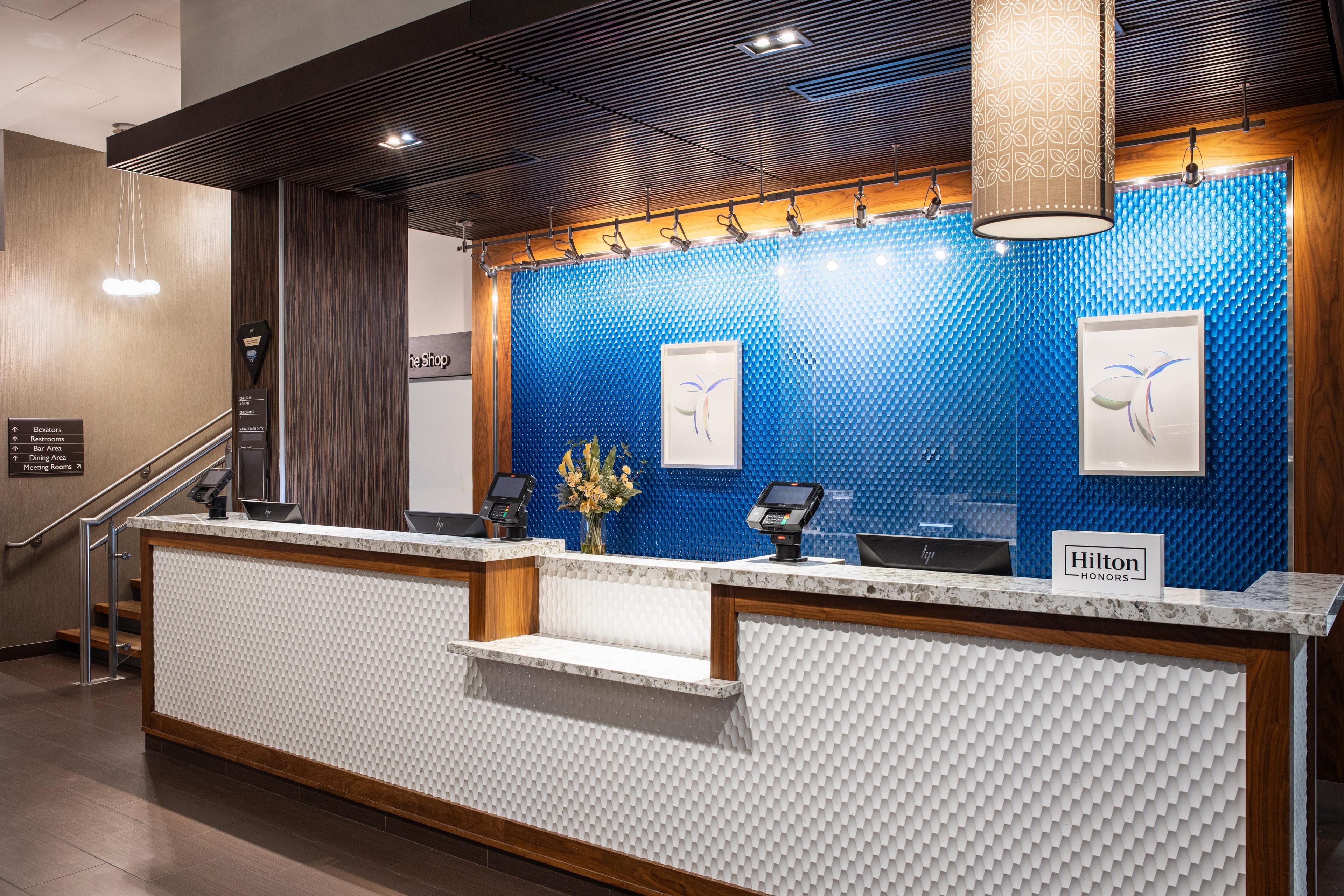 A hotel reception desk with a blue textured wall, a wooden reception desk, and a sign that reads 'Hilton Honors'.
