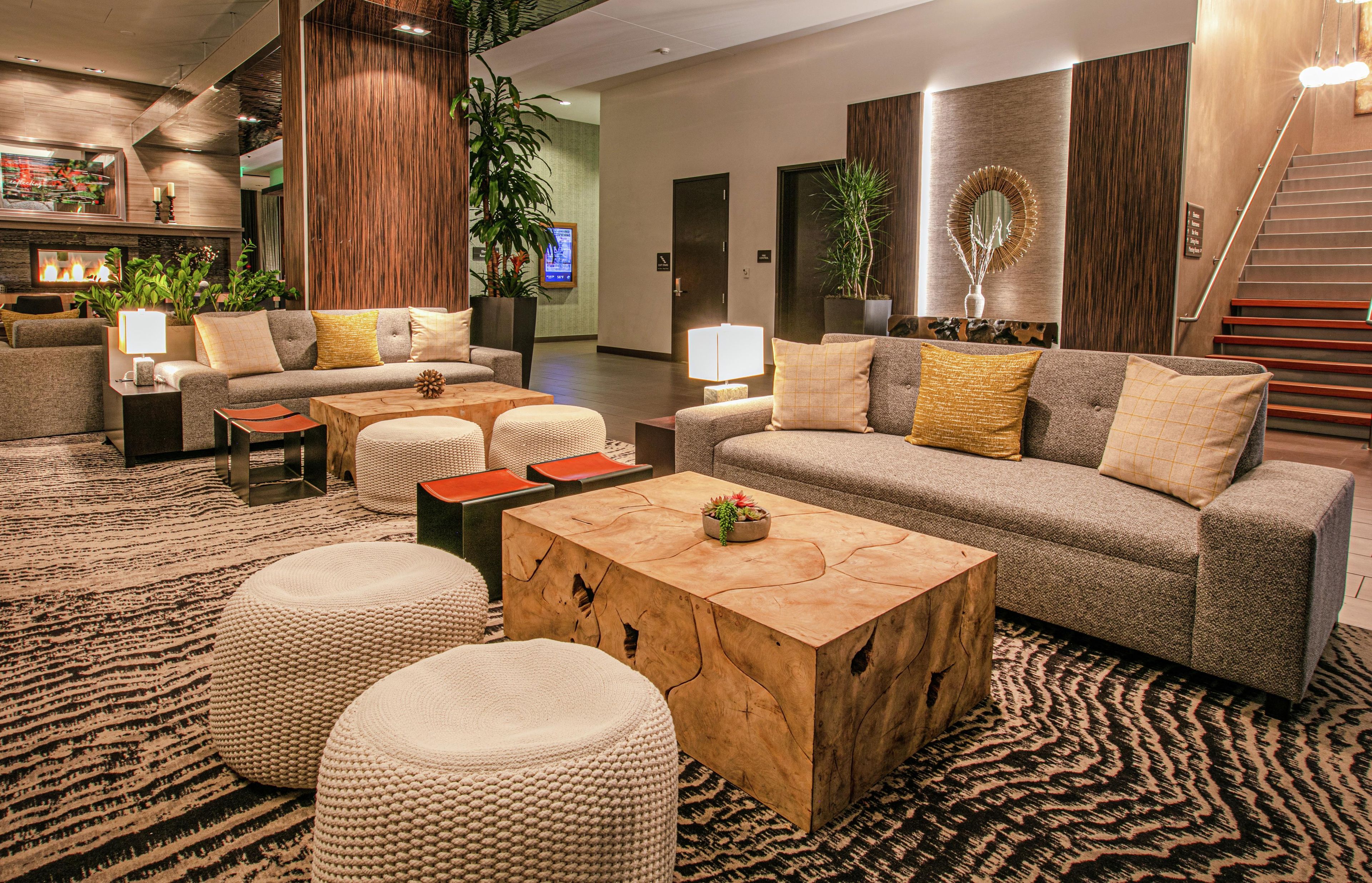 A modern lobby with a sofa set, ottomans, a wooden coffee table, and a patterned carpet.