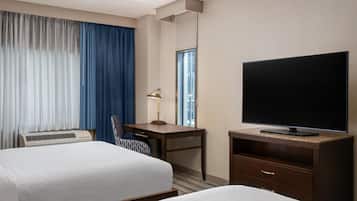 A hotel room with two beds, a desk with a lamp, a television, and an air conditioning unit.