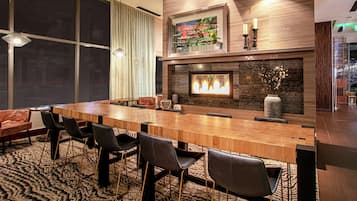 A conference room with a long wooden table, black chairs, a patterned carpet, a fireplace, and a large window.