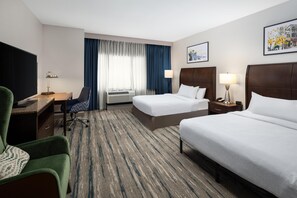 A hotel room with two beds, a desk, a chair, a TV, and a window with curtains.