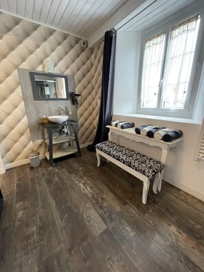 A bathroom with a white sink, a mirror, a bench, and a window with curtains.