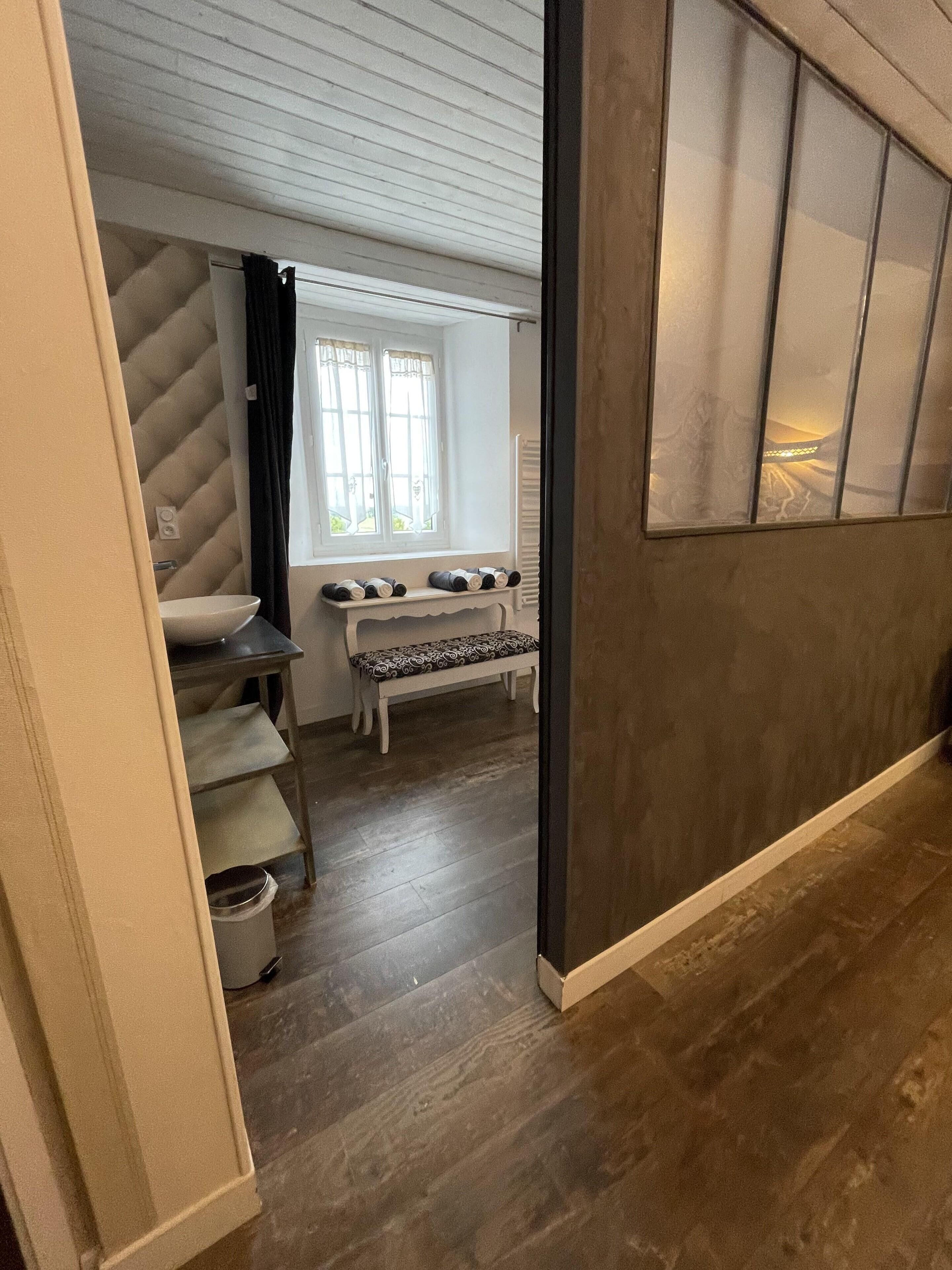 Une salle de bain avec un lavabo blanc, un banc et une fenêtre avec des rideaux.