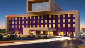 Un hotel moderno con fachada morada, múltiples ventanas y una entrada bien iluminada.