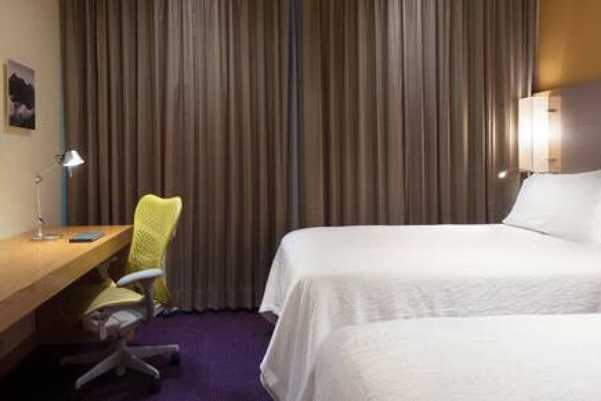 Habitación de hotel con dos camas, un escritorio, una silla y un telón de fondo.