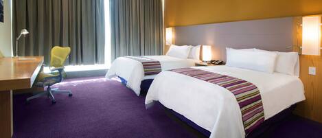 A hotel room with two beds, a desk, a chair, and a large window with curtains.