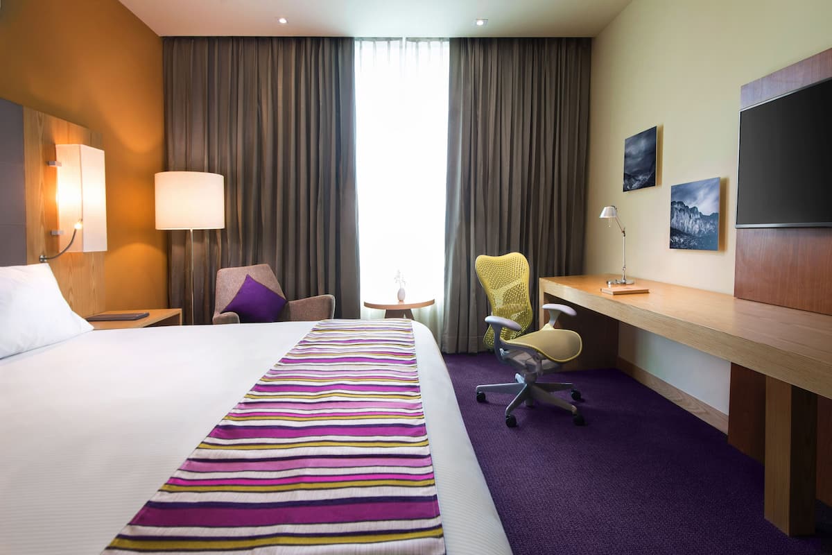 Habitación de hotel con una cama grande, un escritorio, una silla, una mesita y un televisor.