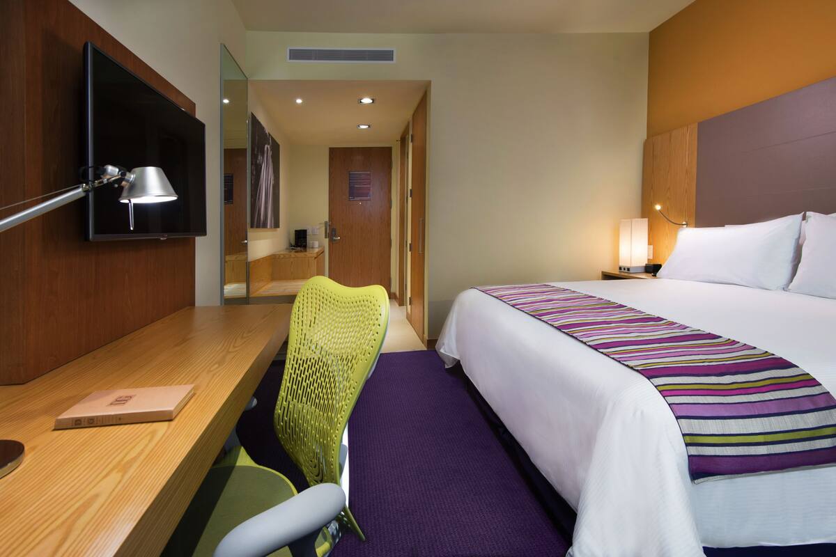 Una habitación de hotel con una cama, un escritorio, una silla, un televisor y una lámpara.