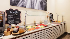 Mostrador de buffet con diversas opciones de comida y letrero de barra de waffles.