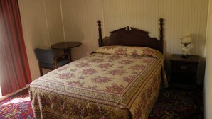 A bedroom with a wooden bed, a small round table, a chair, and a nightstand with a lamp. - Four Jacks Hotel and Casino (Jackpot)