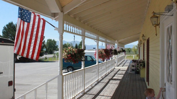 A covered porch with a white railing, a blue vehicle parked in the background, and an American flag. - Four Jacks Hotel and Casino (Jackpot)