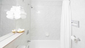Een moderne badkamer met een bad, douche en toilet. Er liggen handdoeken en een mandje op het aanrecht.