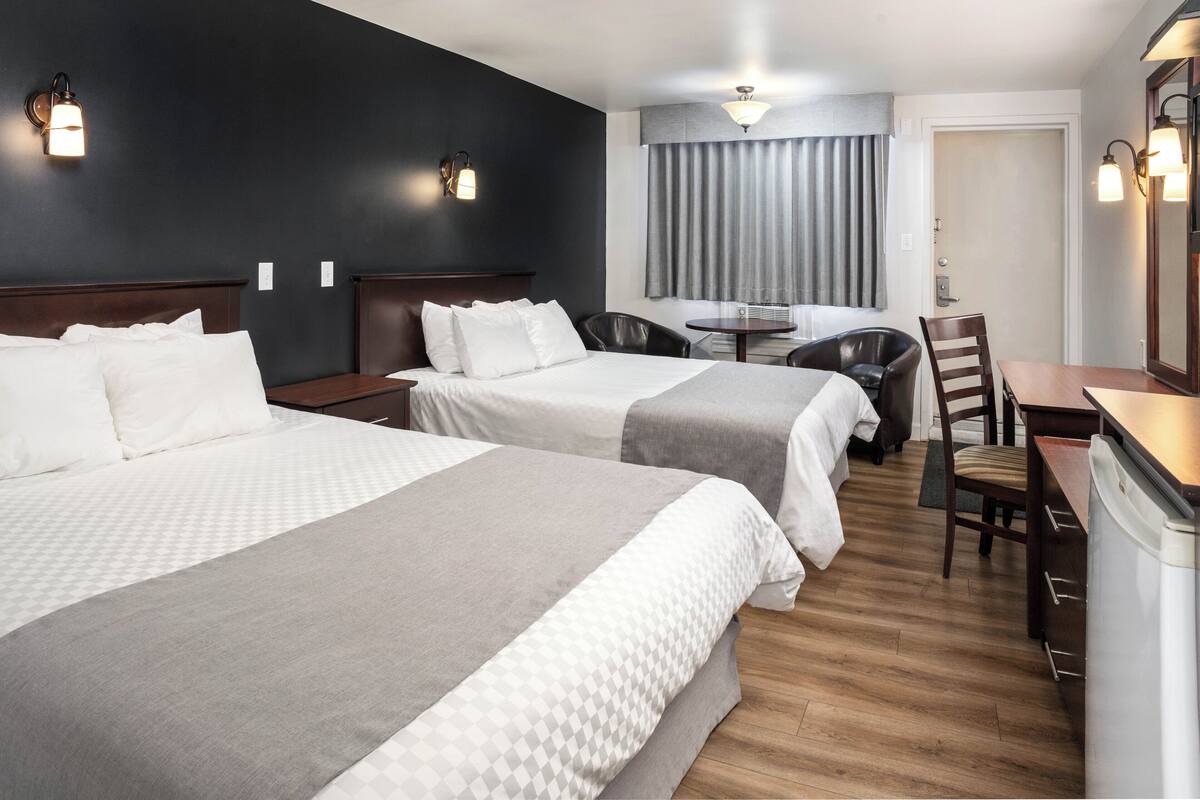 A hotel room with two beds, a desk, a chair, and a small table.