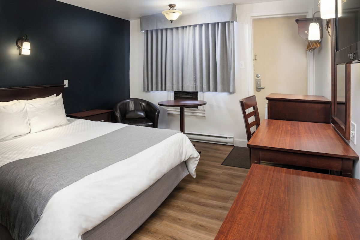 A hotel room with a bed, a desk, a chair, a small table, and a window with curtains.