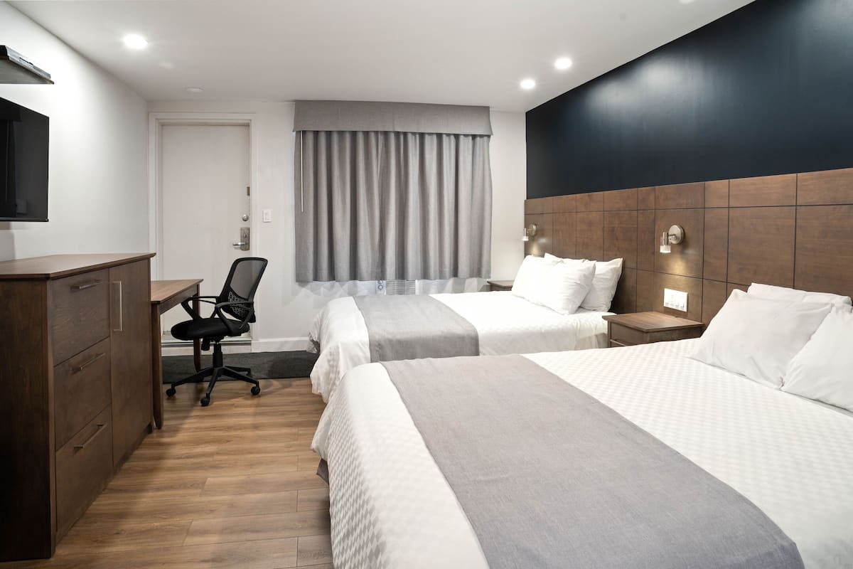 A hotel room with two beds, a desk, and a chair.