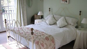 A bedroom with a four-poster bed, two bedside tables with lamps, a floral-patterned bedspread, and a view of the outdoors through a window with curtains. - April Cottage (York)
