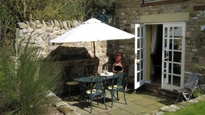 A stone building with a patio area featuring a table and chairs, an open door, and a large white umbrella. - April Cottage (York)
