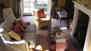 A cozy living room with a sofa, armchairs, a fireplace, and a piano. - April Cottage (York)