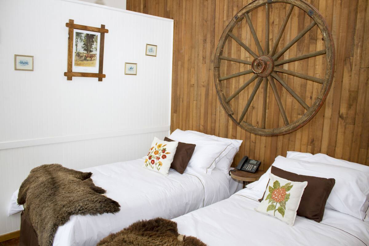 A room with two beds, a wooden wall, and a large wheel.