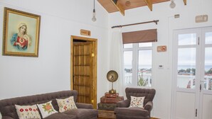 Un salón con un sofá marrón, una puerta de madera, vistas a través de la ventana y un cartel que indica zona para fumadores.