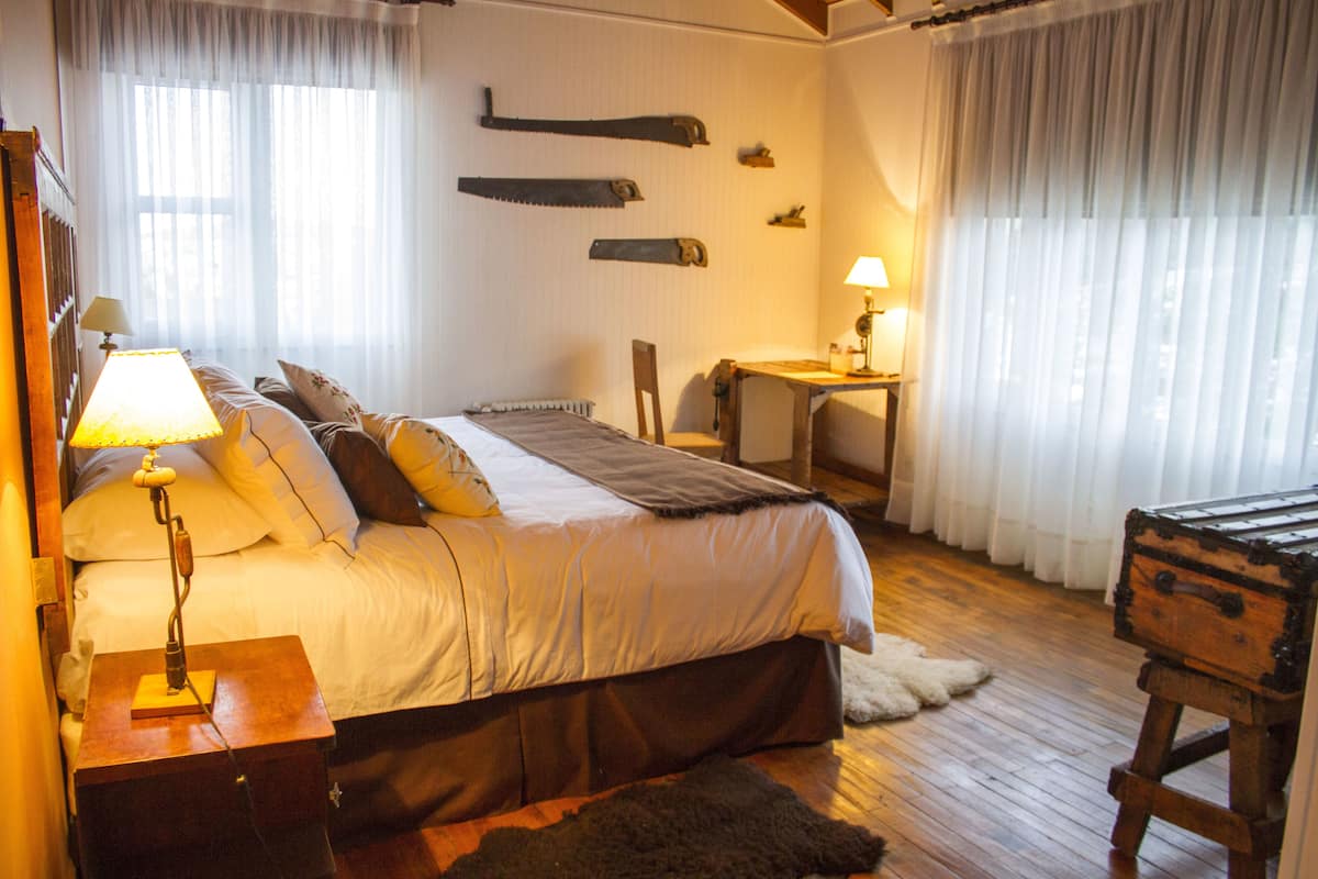 A bedroom with a bed, bedside lamps, a wooden dresser, a chair, and a small table.