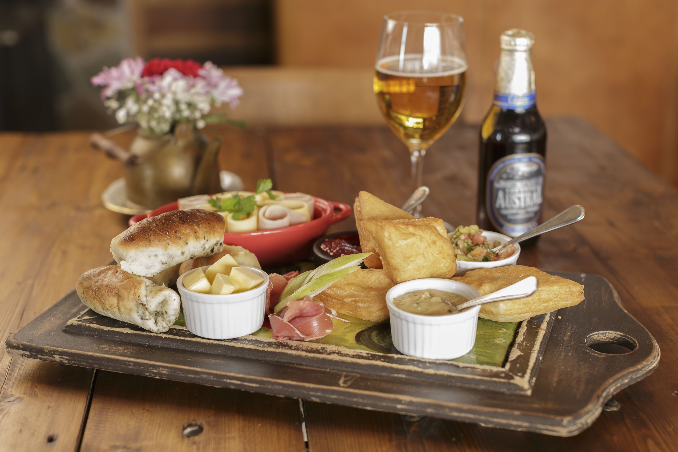 Une table en bois sur laquelle sont disposés divers aliments, notamment du pain, des sauces et une bouteille de bière.