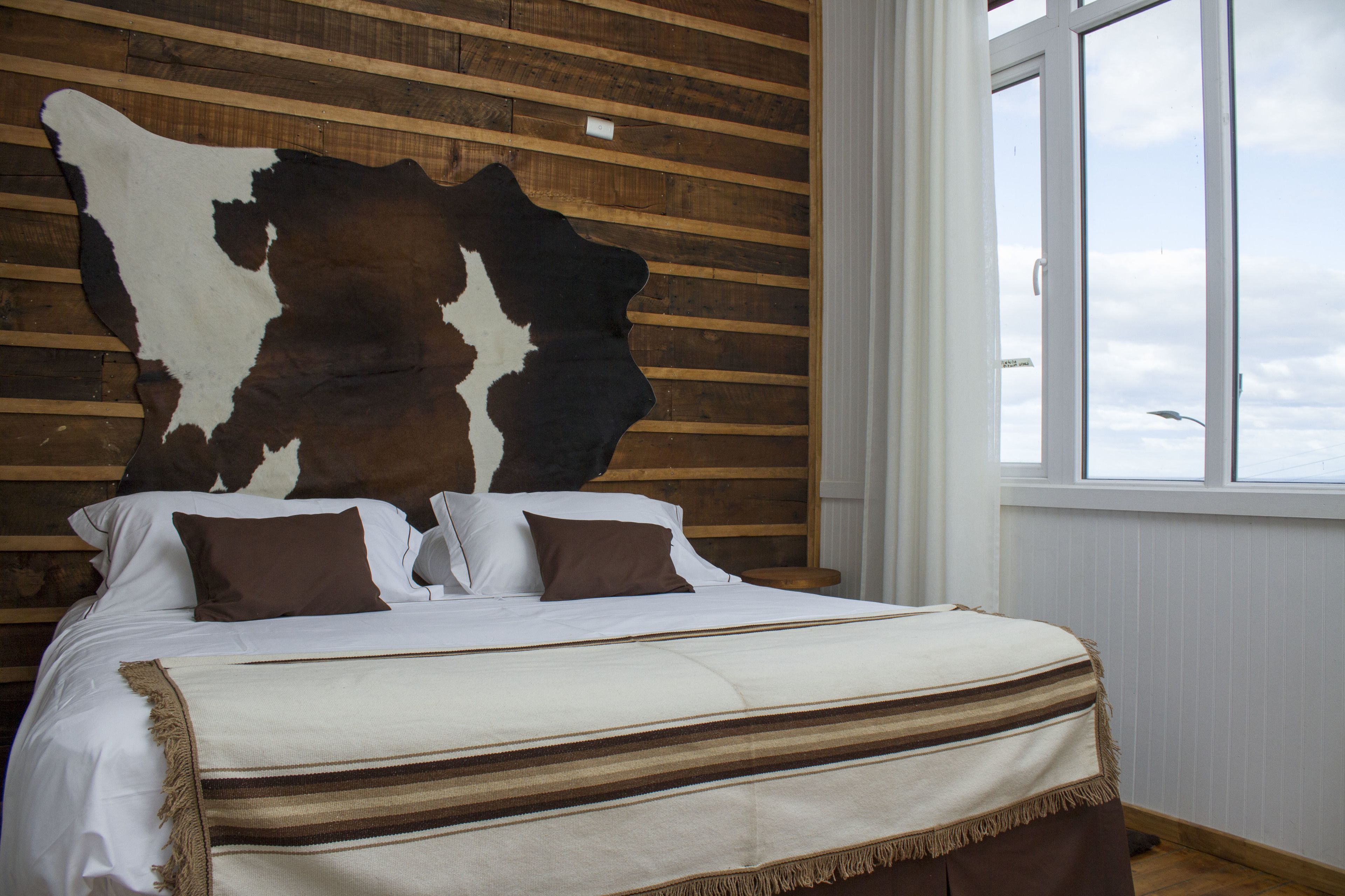 Een bed met een gestreept dekbed, kussens en een groot dierenhuid aan de muur.