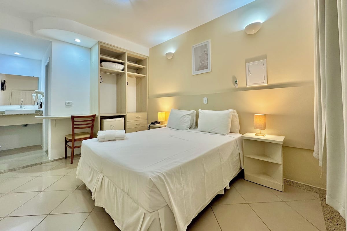 A hotel room with a bed, bedside tables, a desk, and a wardrobe.