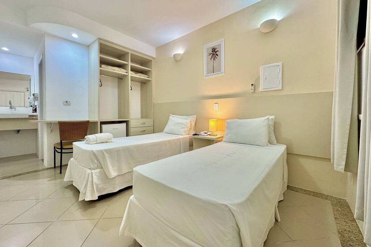 A hotel room with two single beds, a desk, a chair, a wardrobe, and a bathroom.