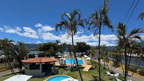 A pool area with a circular pool, lounge chairs, umbrellas, and palm trees. - Hotel Recanto dos Pássaros (São Sebastião)