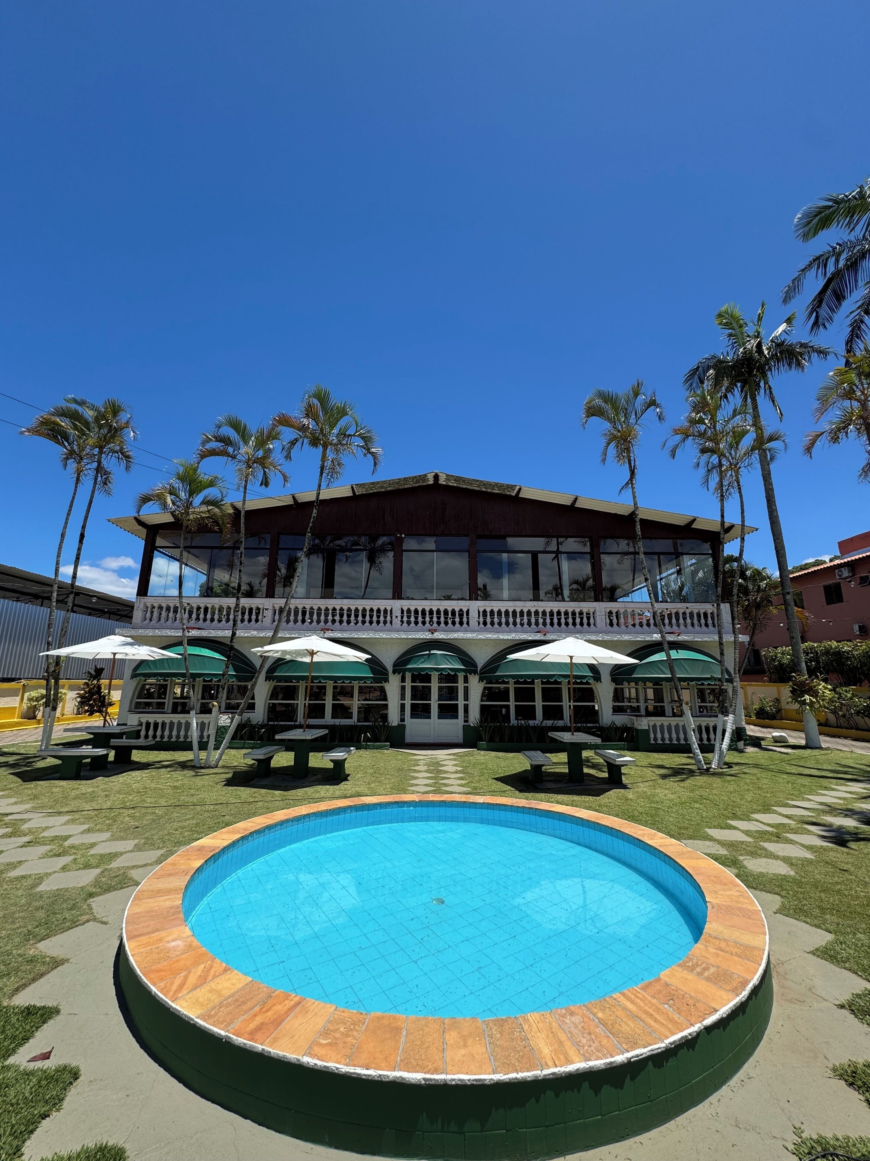 A pool with a wooden deck, a building with a balcony, and palm trees.