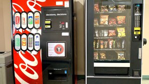 Deux distributeurs automatiques : l’un arbore le logo Coca-Cola, l’autre propose une variété de collations.