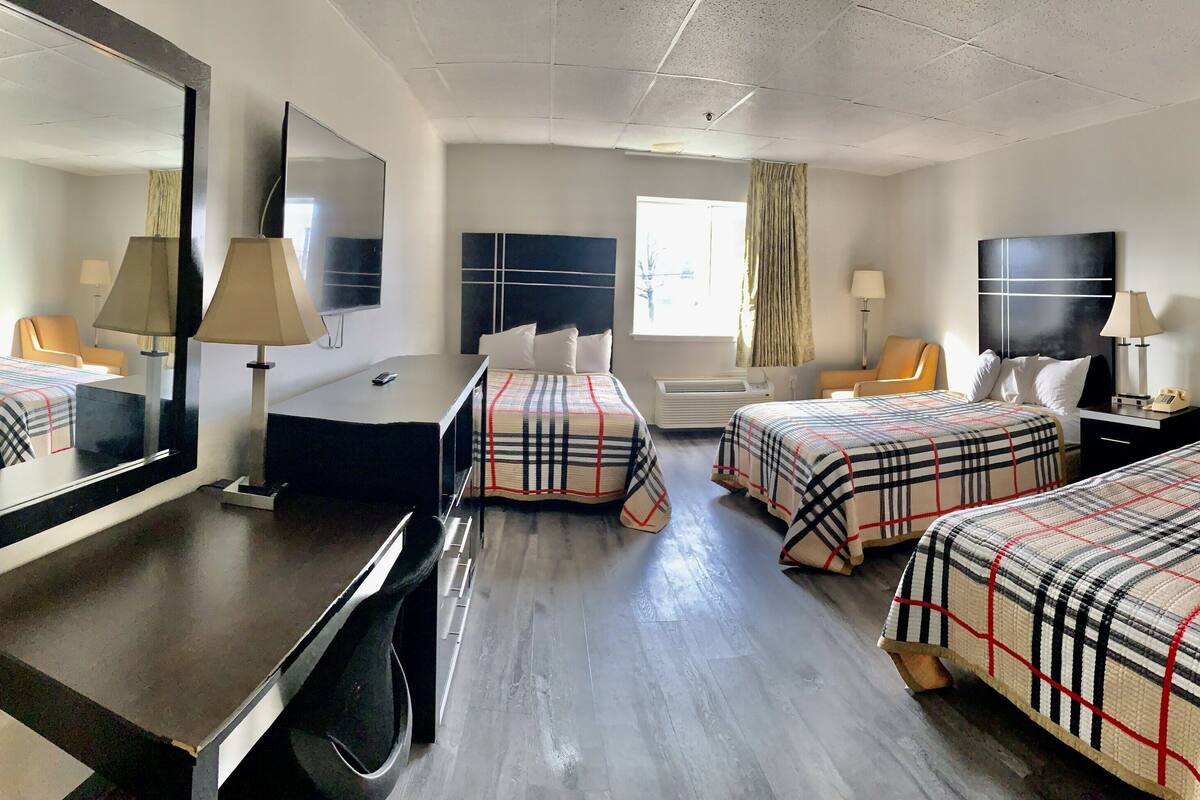 A hotel room with two beds, a desk, a TV, and a mirror.