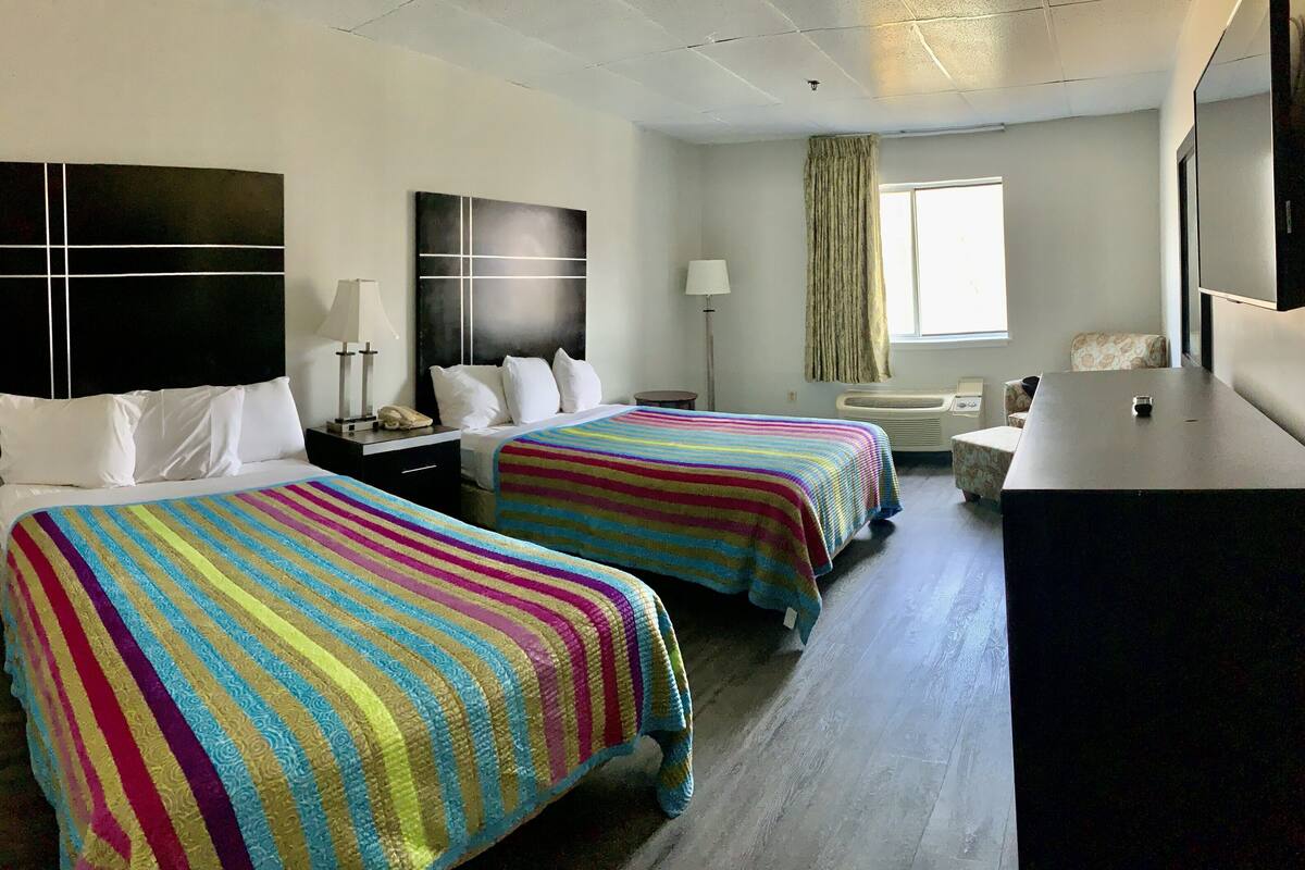 A hotel room with two beds, a desk, a chair, a window, and a TV.