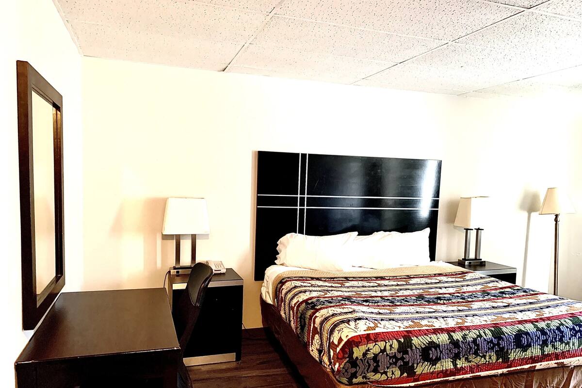 A hotel room with a bed, a desk, two bedside tables with lamps, and a large mirror on the wall.