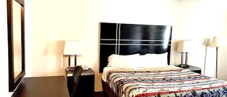 A hotel room with a bed, a desk, two bedside tables with lamps, and a large mirror on the wall.