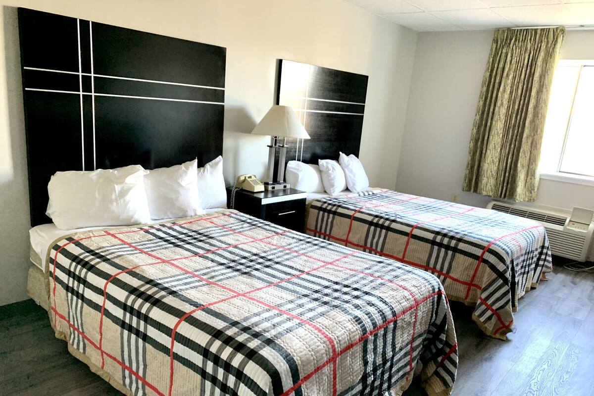 A hotel room with two beds, a nightstand, a lamp, and a window with curtains.