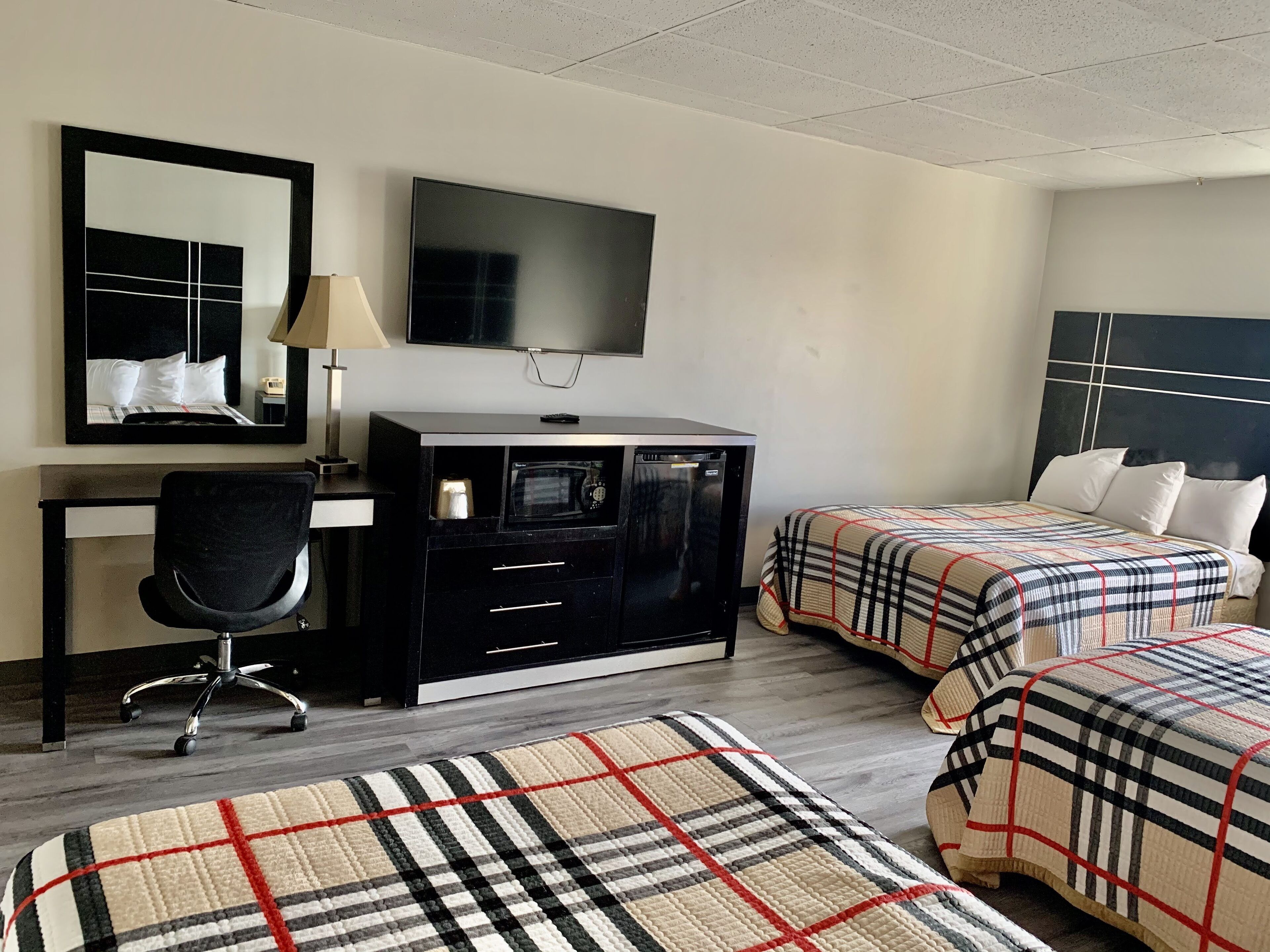 Habitación de hotel con cama, escritorio, silla, televisor, microondas y cómoda.