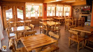 A rustic wooden interior with multiple tables and chairs, large windows with curtains, and a television on the wall. - Hotel Taramuri (Bocoyna)
