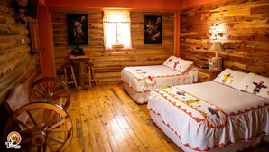 A cabin-style room with two beds, a wooden wheel chair, a small table, and a window with curtains. - Hotel Taramuri (Bocoyna)