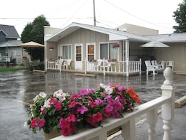 Um motel com área de estar coberta, varanda com grades brancas e floreiras.